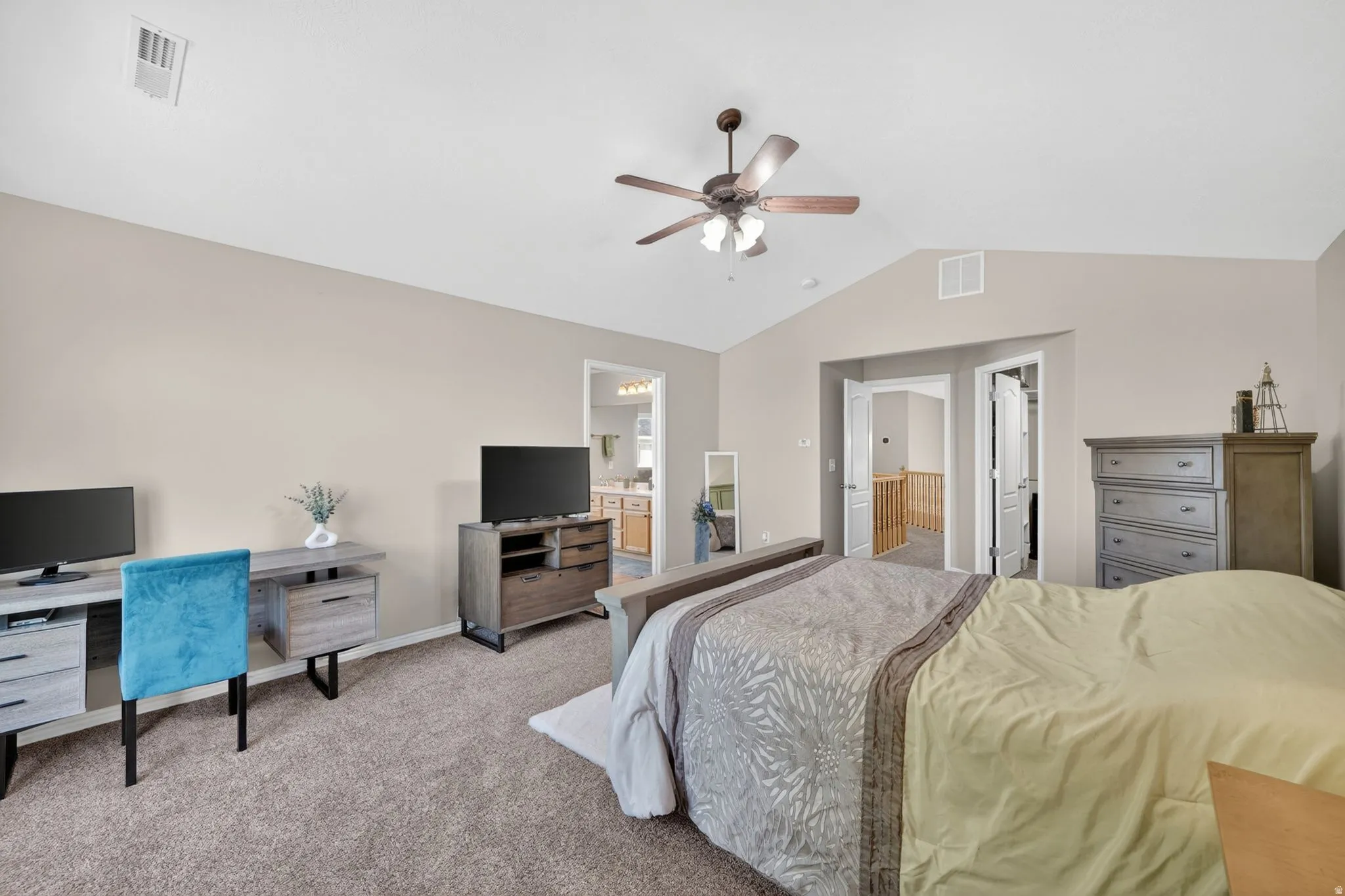 Spacious carpeted room featuring a vaulted ceiling with a ceiling fan, light-toned walls, and an open doorway leading to a bathroom with a vanity