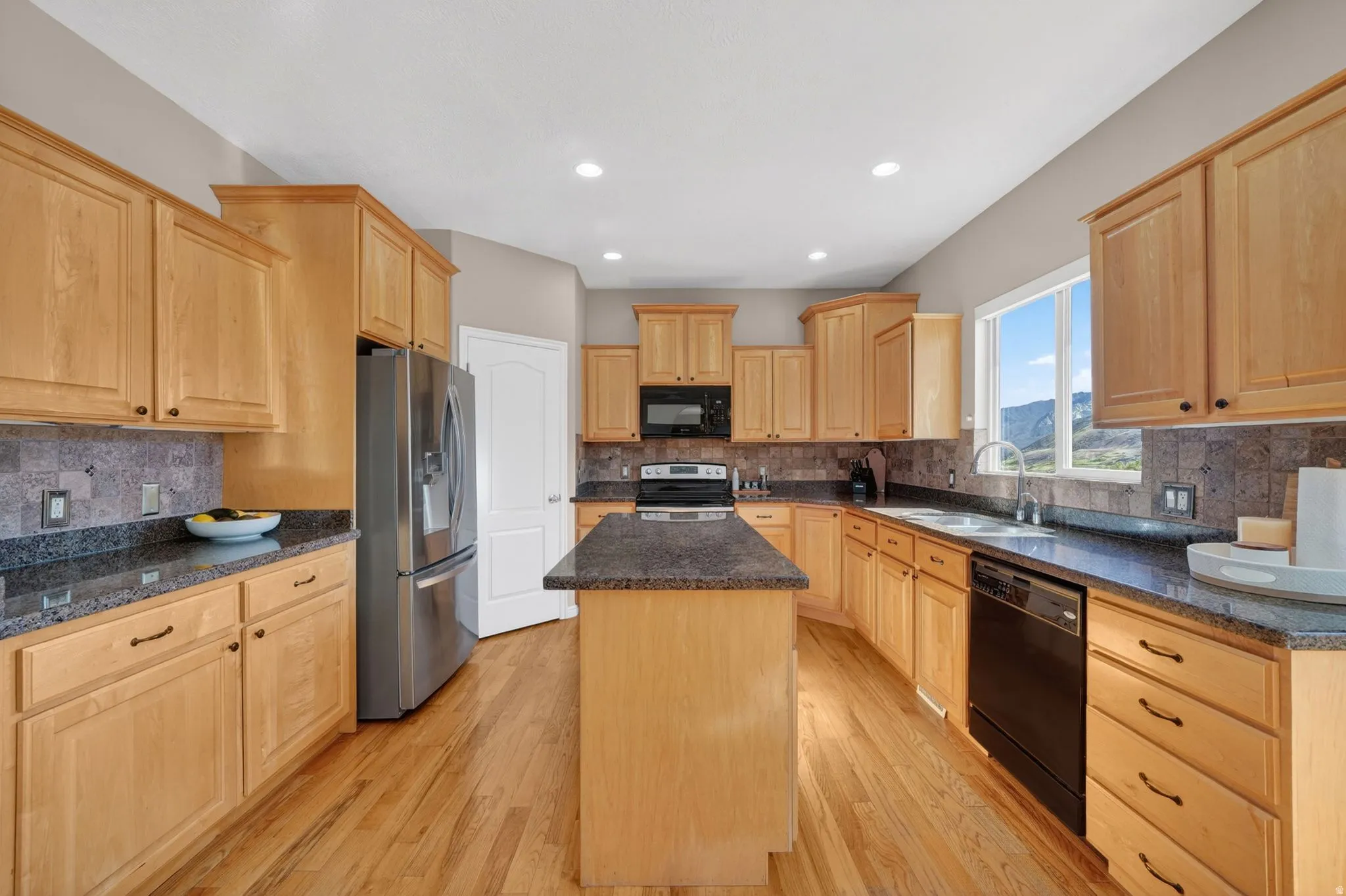 Kitchen with wood cabinetry, dark countertops, stainless steel refrigerator, and integrated black appliances