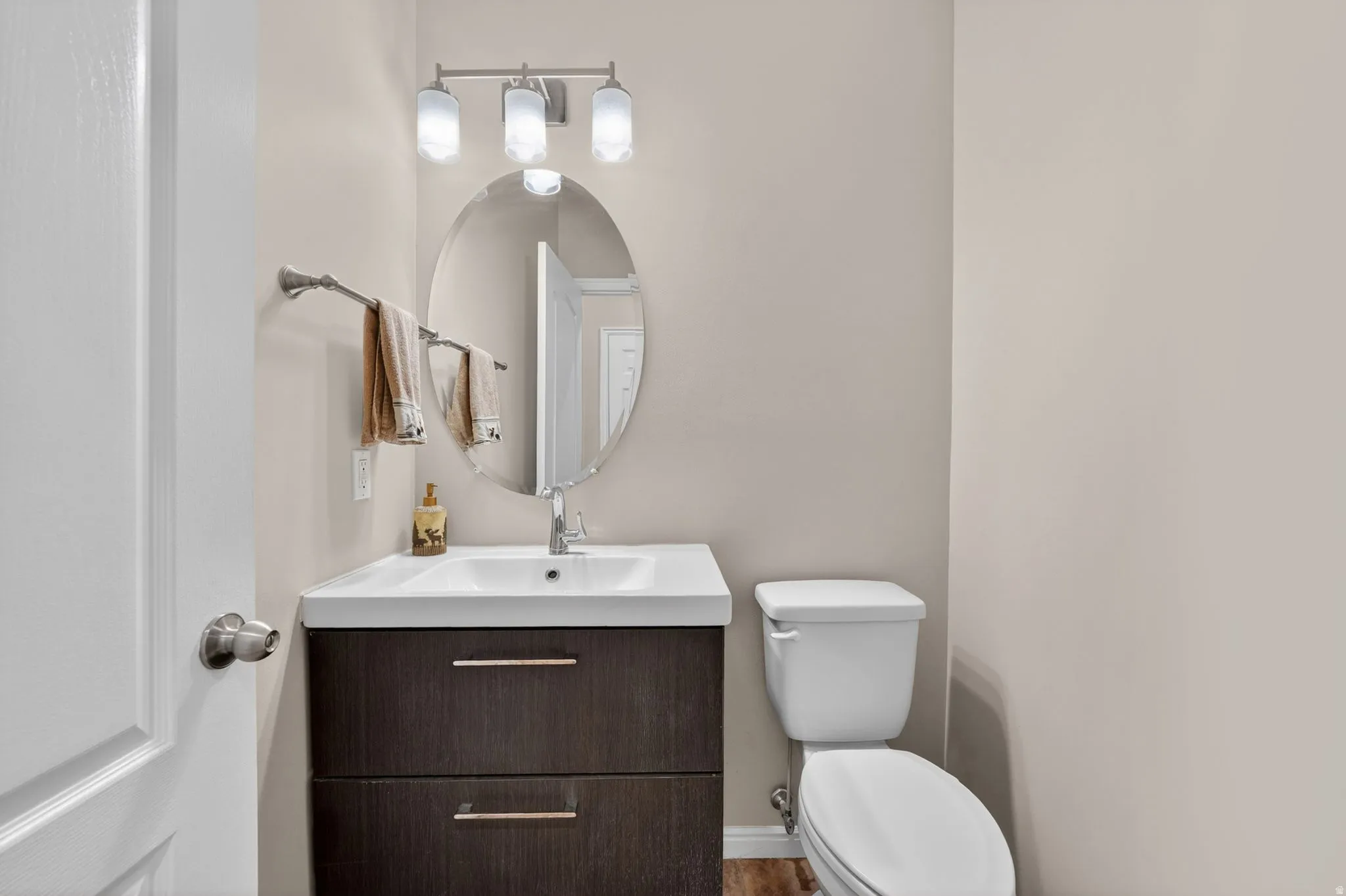 Bathroom featuring a contemporary floating vanity with an integrated sink, a dark wood-finish cabinet with two drawers, an oval mirror, and a three-light vanity fixture