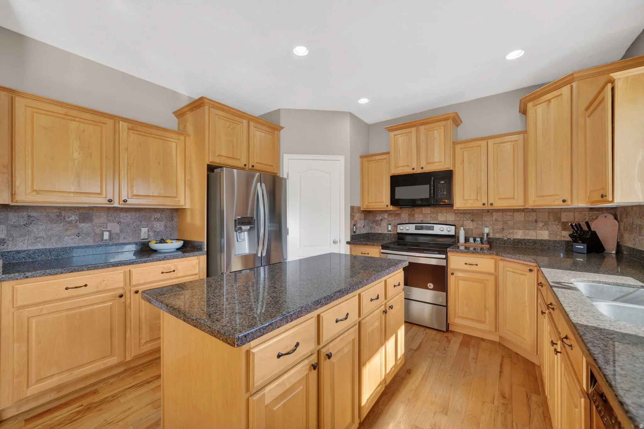 Kitchen featuring a central island with a stone countertop, light wood cabinetry, stainless steel appliances, and wood-finish flooring