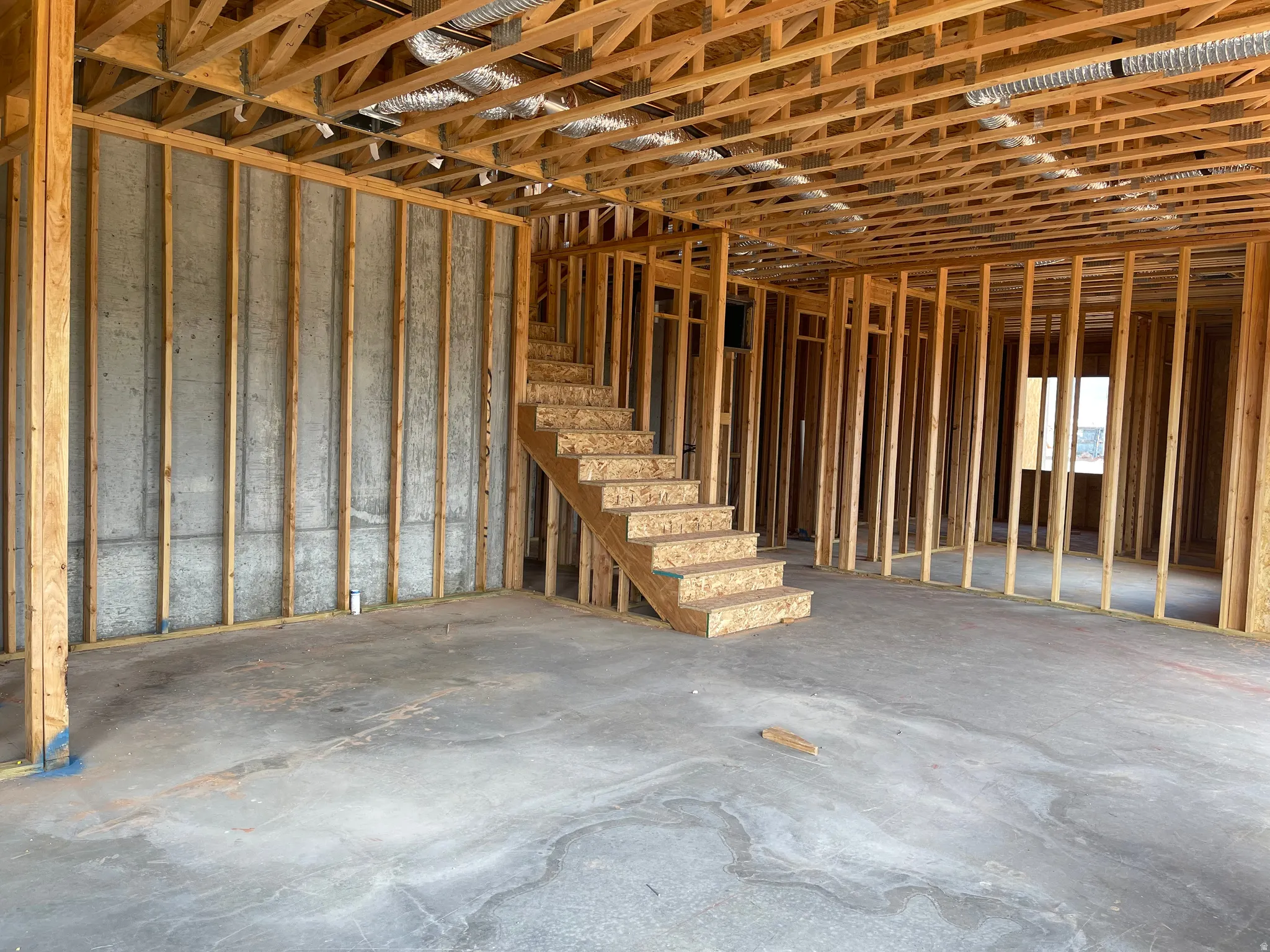 Unfinished interior space featuring exposed wood framing, a concrete slab floor, and an unfinished staircase
