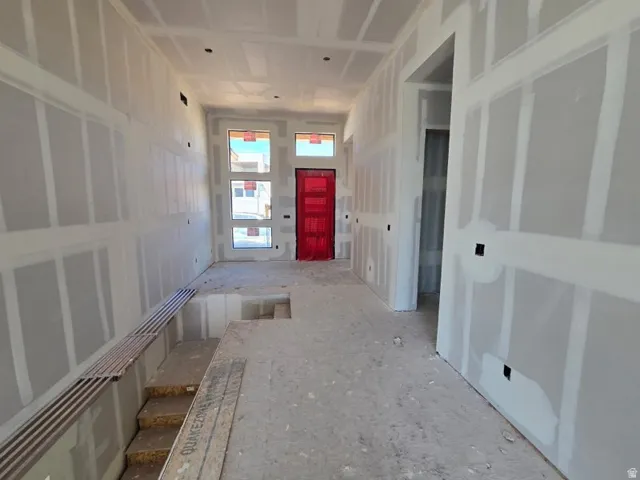 Drywall-finished walls and ceiling, red-painted entry door, and multiple tall windows provide natural light
