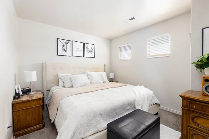 Carpeted bedroom with light-toned walls and two windows featuring horizontal blinds