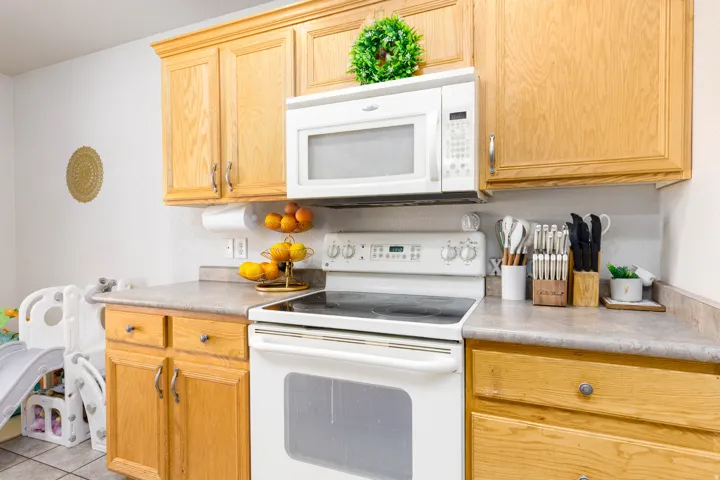 Kitchen featuring a white electric range, an over-the-range microwave, light wood cabinetry, and a light-toned countertop