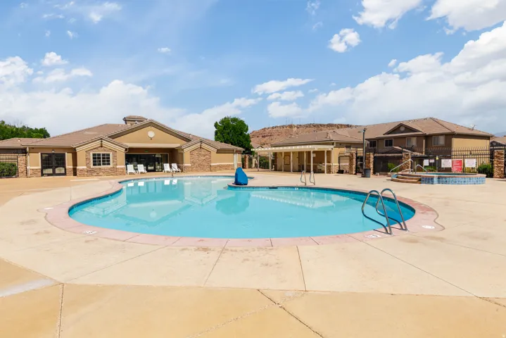 Resort-style pool area featuring a large, irregularly shaped swimming pool, expansive concrete decking, and a separate raised spa