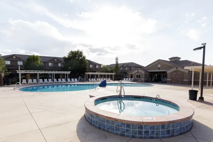 Outdoor swimming pool with integrated hot tub, extensive concrete decking, and multiple lounge chairs