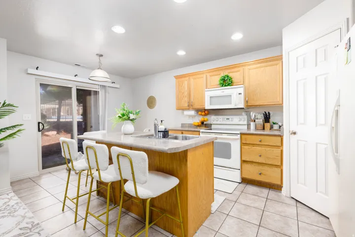 Kitchen with light wood cabinetry, white appliances, and a central island with an integrated sink