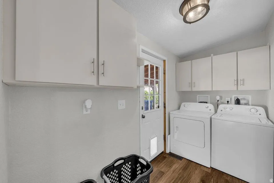 Dedicated laundry area featuring wood-finish flooring and multiple upper cabinets
