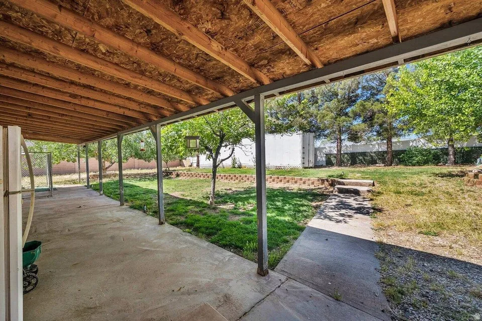 Spacious covered patio with a concrete surface and a wood-finish ceiling, extending to a landscaped yard with mature trees and a concrete pathway