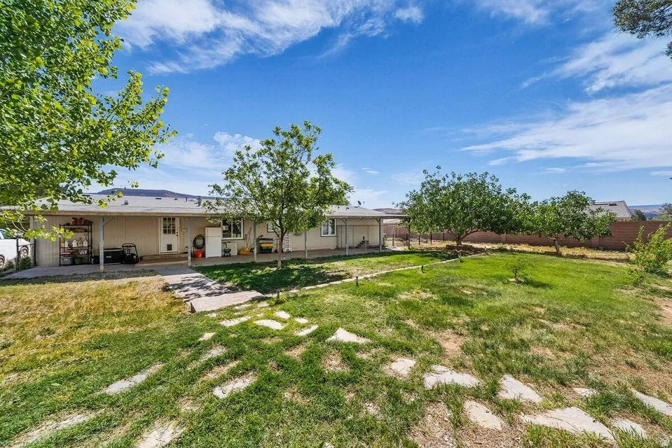 Expansive backyard featuring a shaded patio, mature trees, green lawn, stone pathway, and privacy fencing