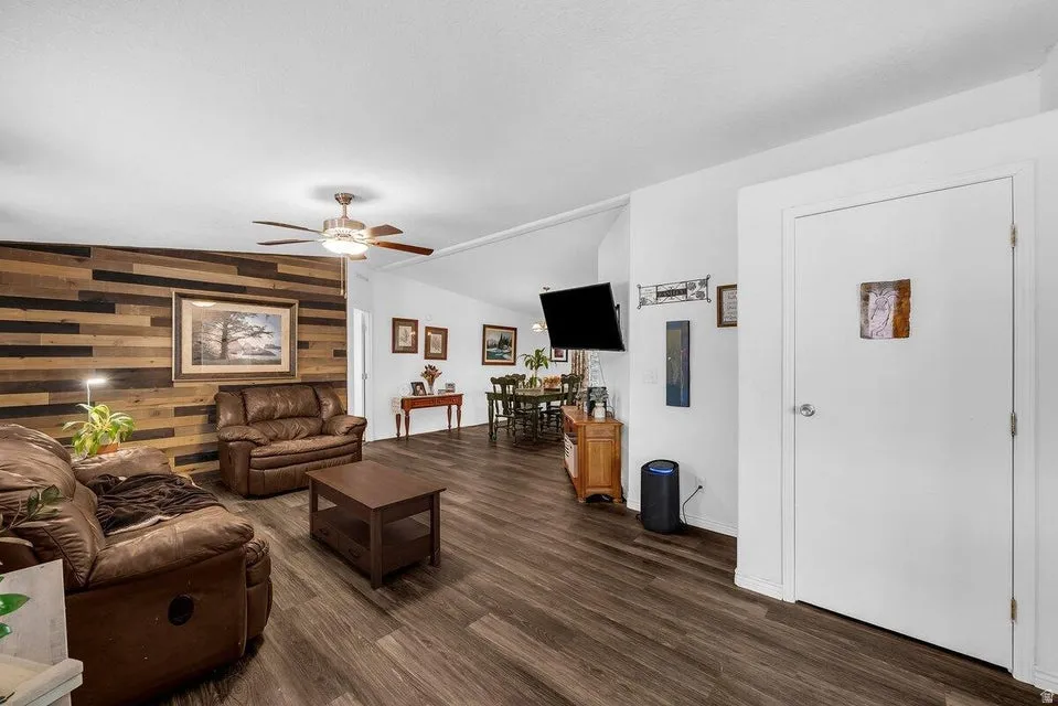 Living area featuring wood-finish flooring, a decorative wood accent wall, and an overhead ceiling fan with integrated lighting