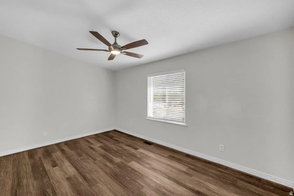 Spacious room featuring wood-finish flooring, light-colored walls, and a ceiling fan with integrated lighting