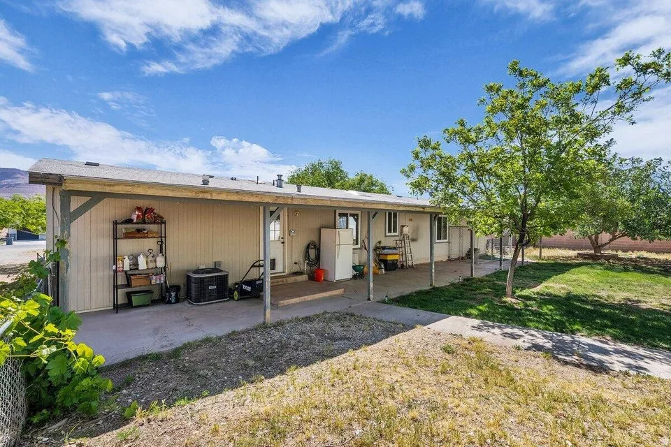 Rear exterior featuring an extended covered patio, concrete walkway, and a partial chain-link fence