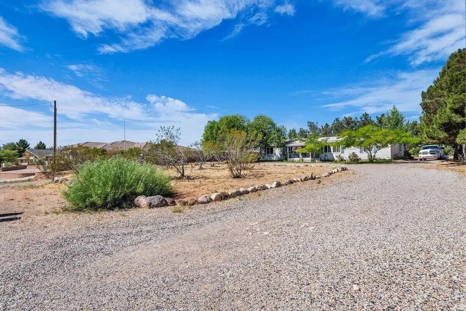 Gravel driveway opening to a single-story residence with a light-colored exterior and surrounding trees
