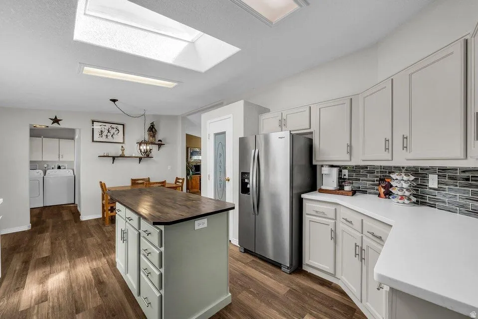 Kitchen featuring a central island with wood-finish countertop, light gray cabinetry, stainless steel refrigerator, and mosaic tile backsplash