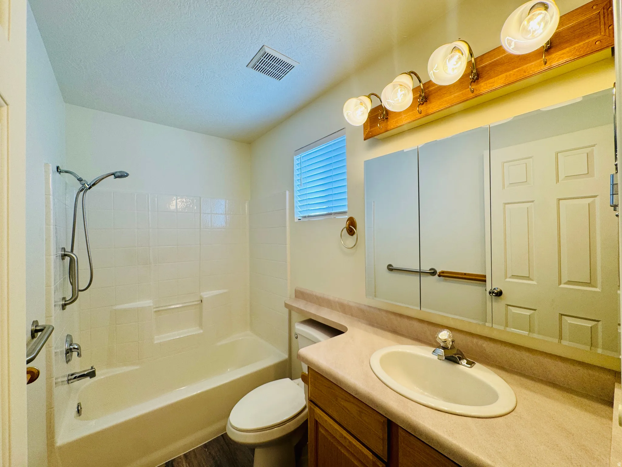 Full bathroom featuring a tub/shower combination with white subway tile surround, a single vanity with an integrated sink, a large mirror, and wood-finish flooring
