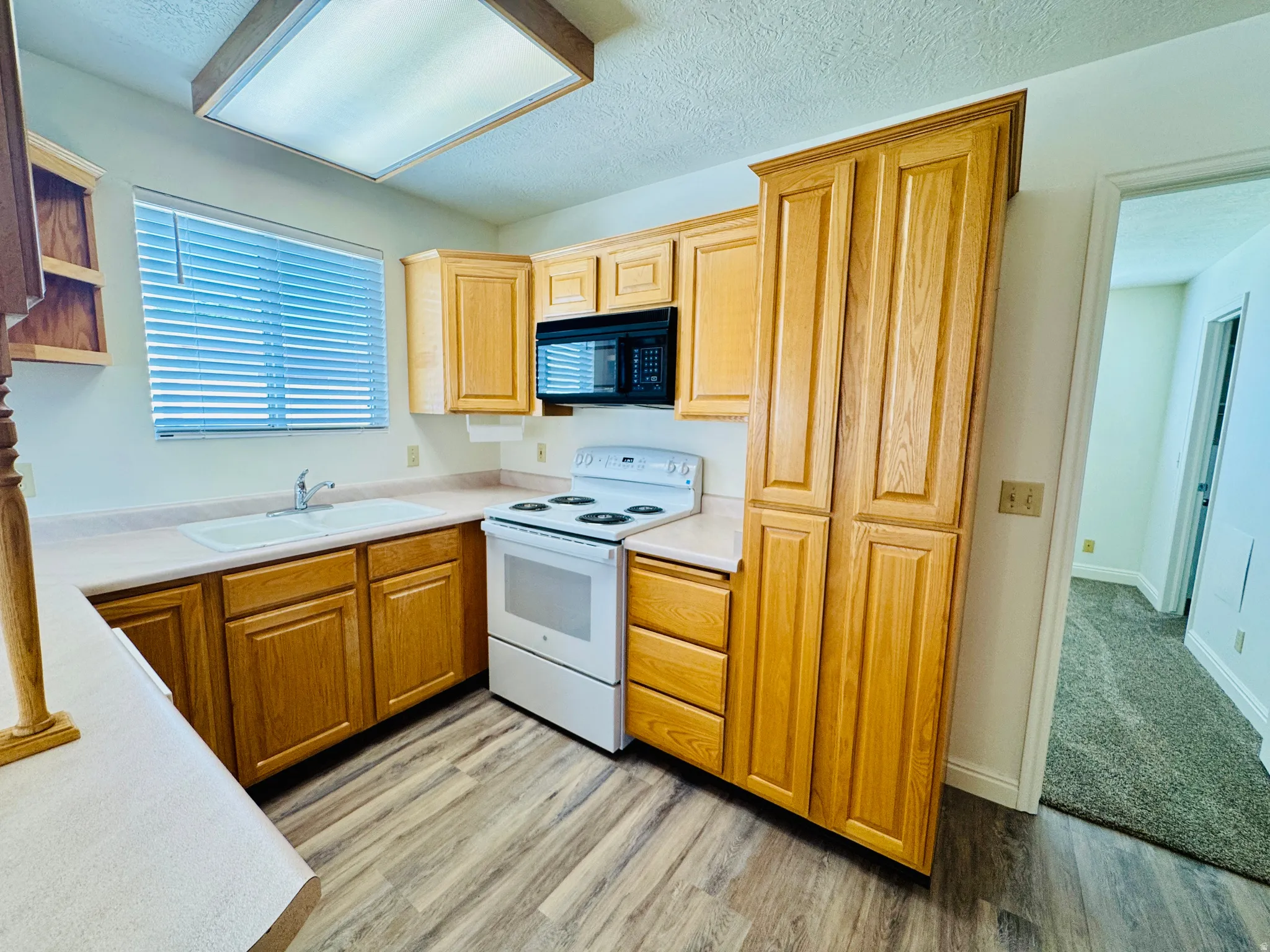 Kitchen featuring wood-finish flooring, wood cabinetry, built-in microwave, white electric range, and a double basin sink
