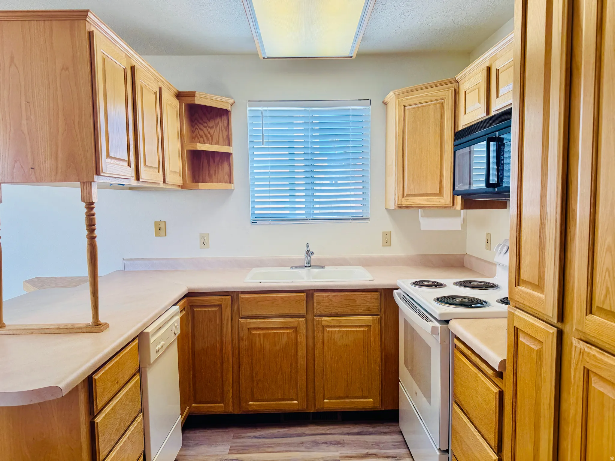 Kitchen featuring wood-finish cabinetry, a white built-in dishwasher, and a white electric range