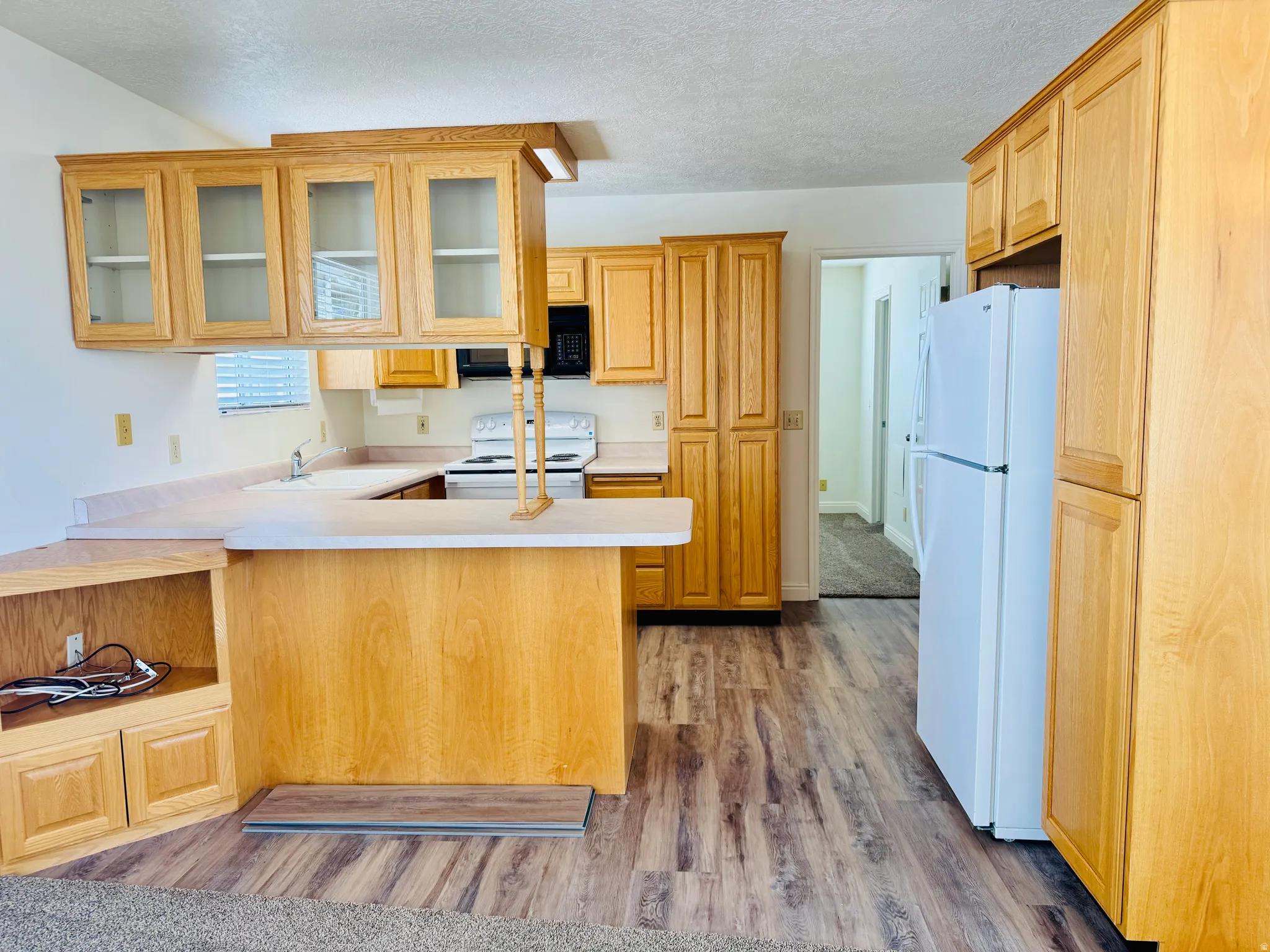 Kitchen featuring wood-finish flooring, light-toned cabinetry with some upper glass-front doors, white appliances, and a built-in breakfast bar