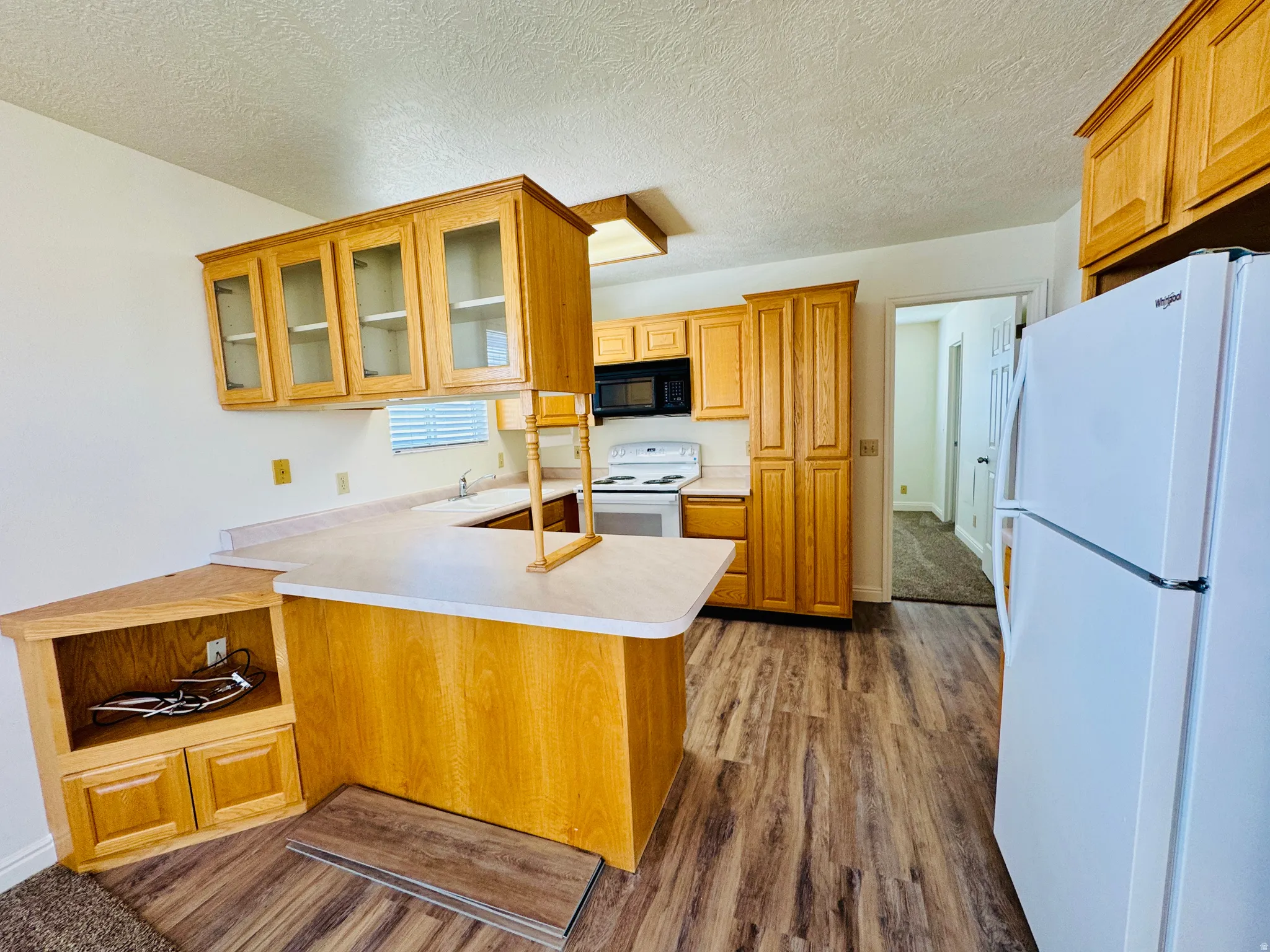 Kitchen featuring wood-finish flooring, light wood cabinetry, white countertops, and a white appliance suite including a refrigerator, range, and microwave