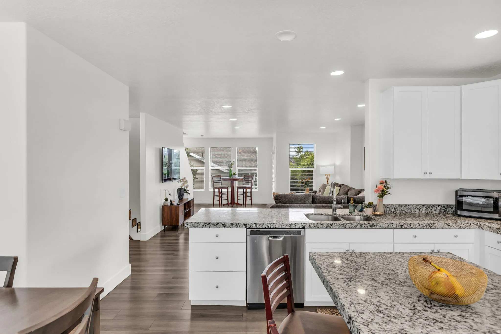 Kitchen featuring white cabinetry, stainless steel dishwasher, double basin sink with a gooseneck faucet, light-toned granite countertops, and wood-finish flooring
