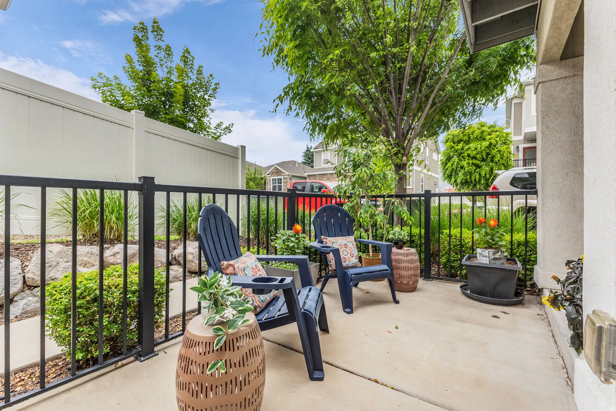 Concrete patio area featuring a black metal railing, private vinyl fencing, and mature landscaping