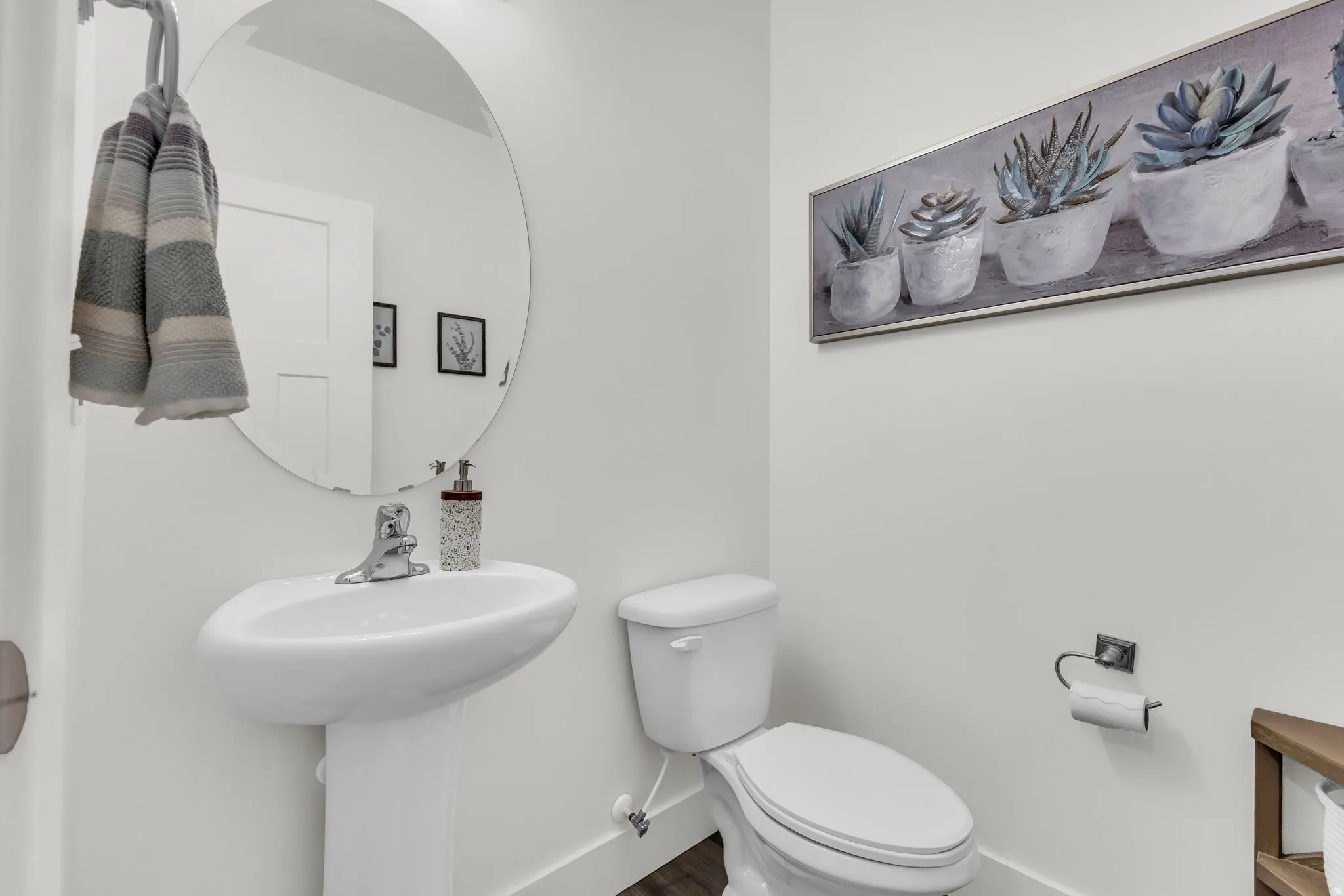 Bright white powder room featuring a pedestal sink with a chrome faucet, a round wall-mounted mirror, just off the living area.