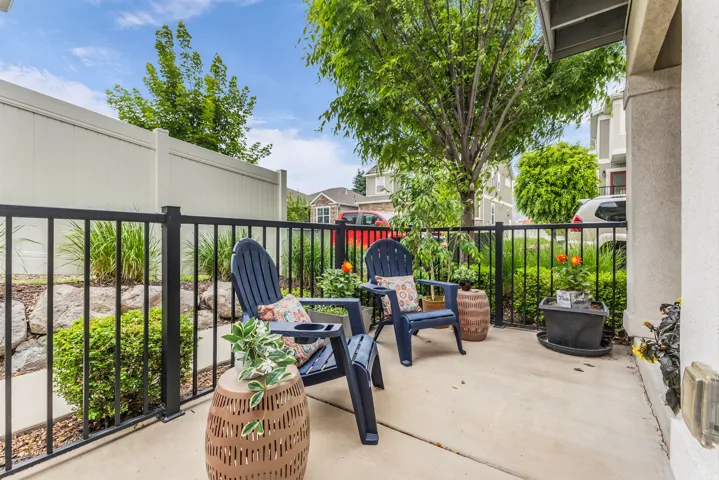 Concrete patio area featuring a black metal railing, private vinyl fencing, and mature landscaping