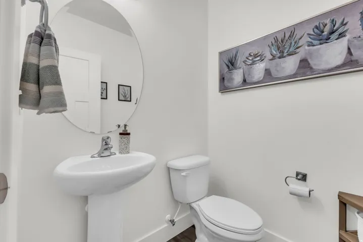 Bright white powder room featuring a pedestal sink with a chrome faucet, a round wall-mounted mirror, just off the living area.