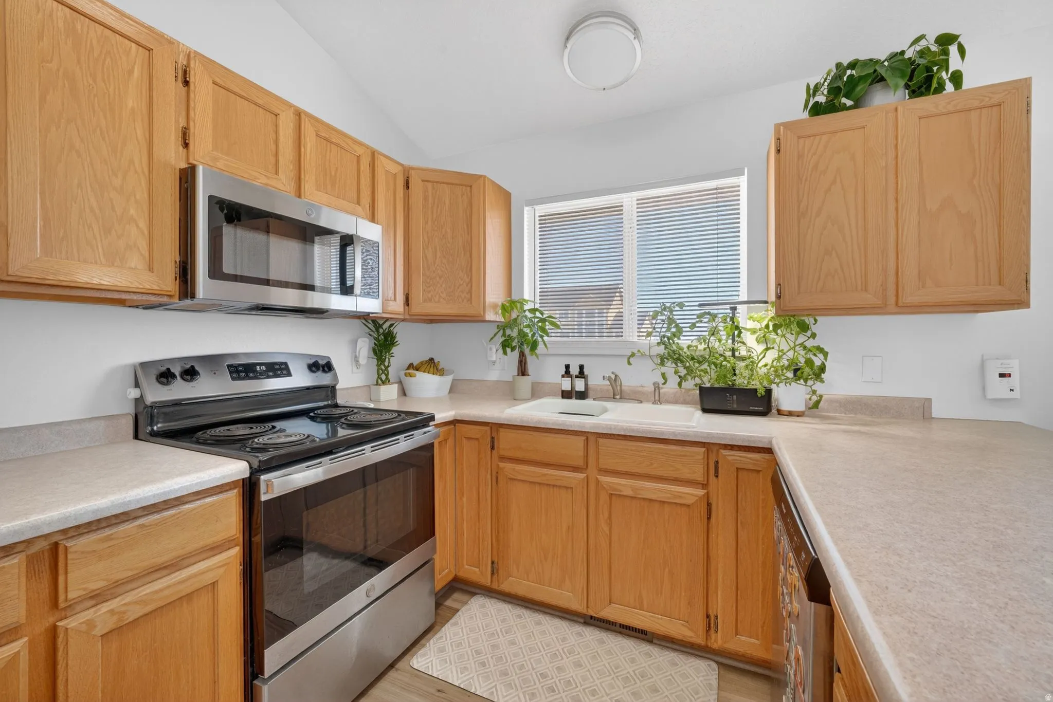 Kitchen featuring wood cabinetry, stainless steel appliances, a double basin sink, and a window with blinds