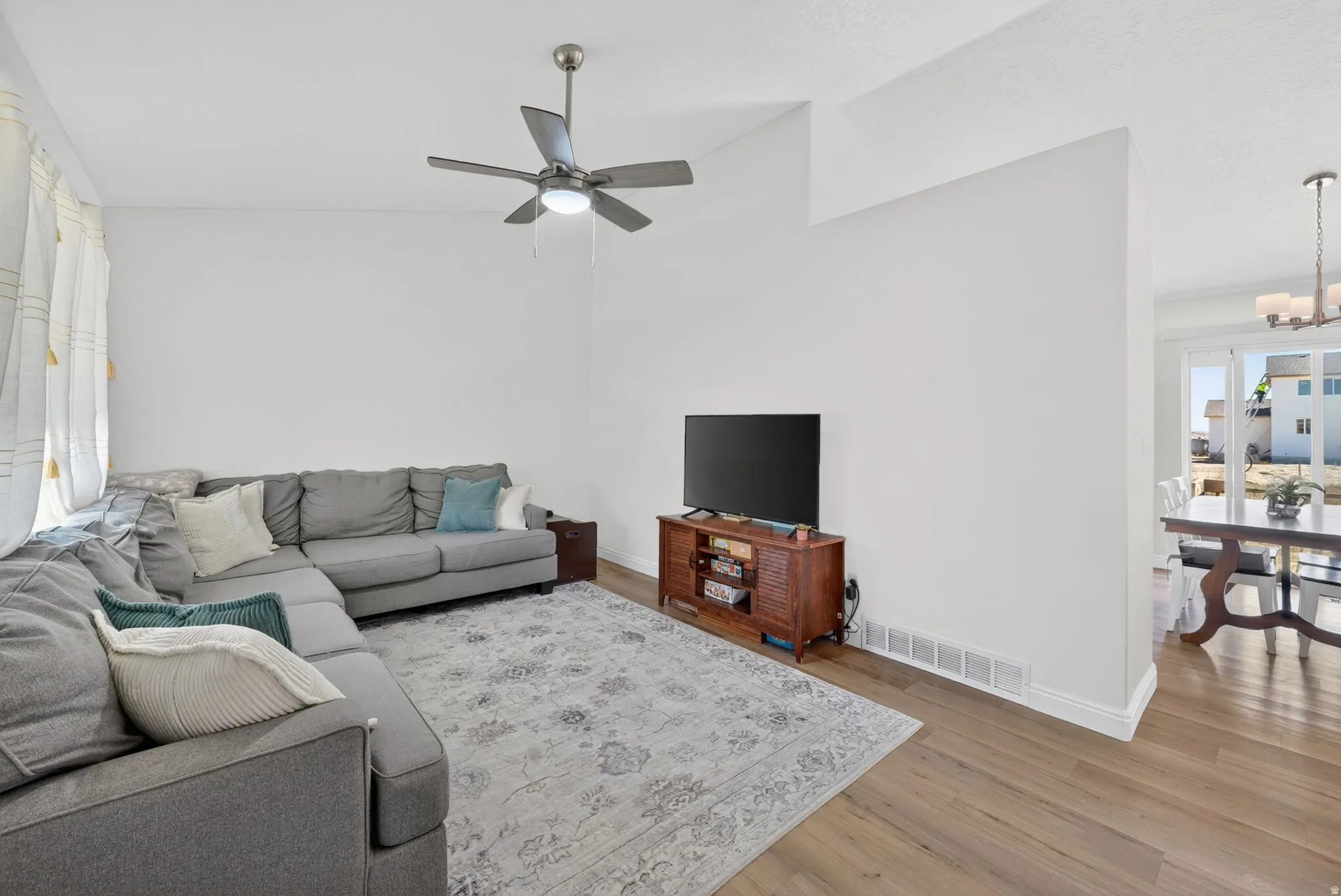 Living area with wood-finish flooring, vaulted ceiling, and a ceiling fan with integrated lighting