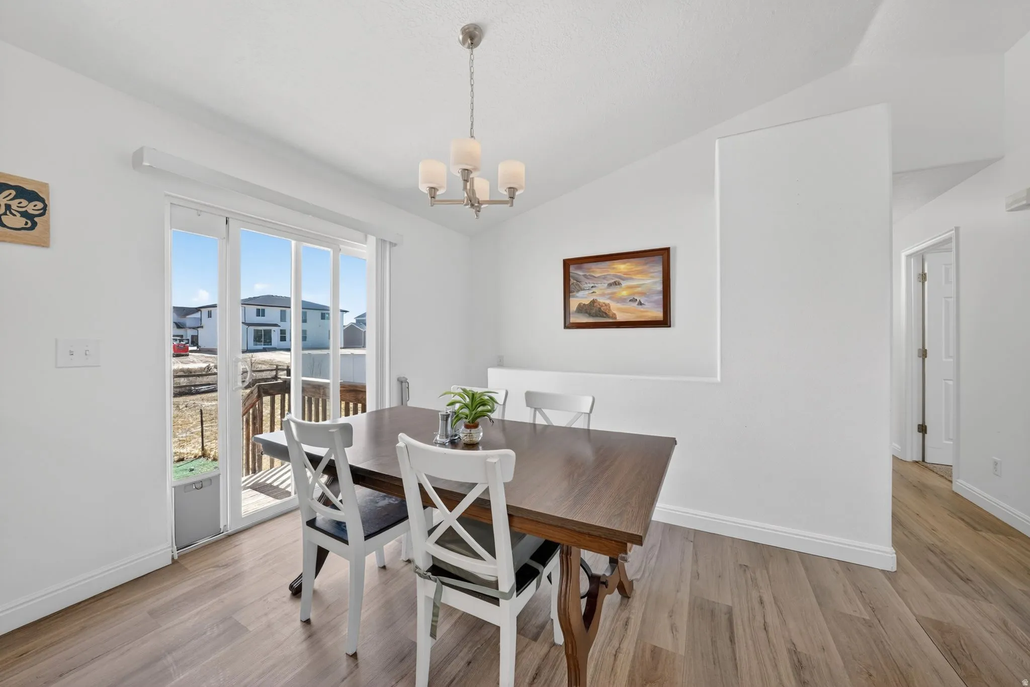 Dining space featuring wood-finish flooring, white walls, and a contemporary chandelier