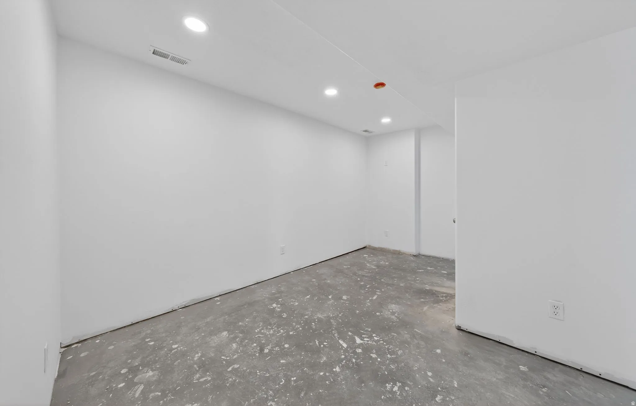 Spacious room with white painted walls, recessed lighting, and a concrete floor