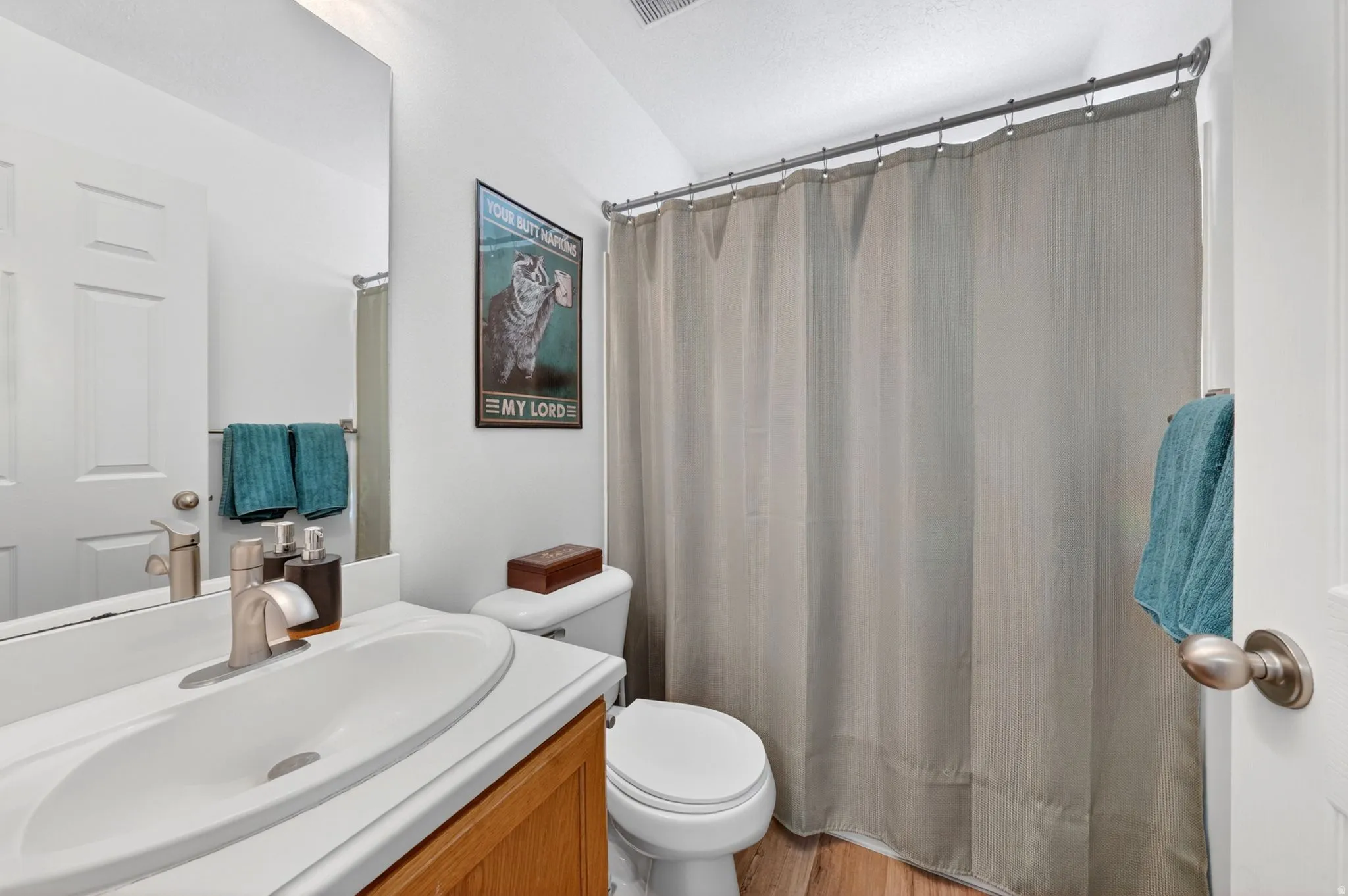 Bathroom featuring a single vanity with an integrated sink and brushed nickel faucet, a toilet, and a shower/tub combination with a shower curtain