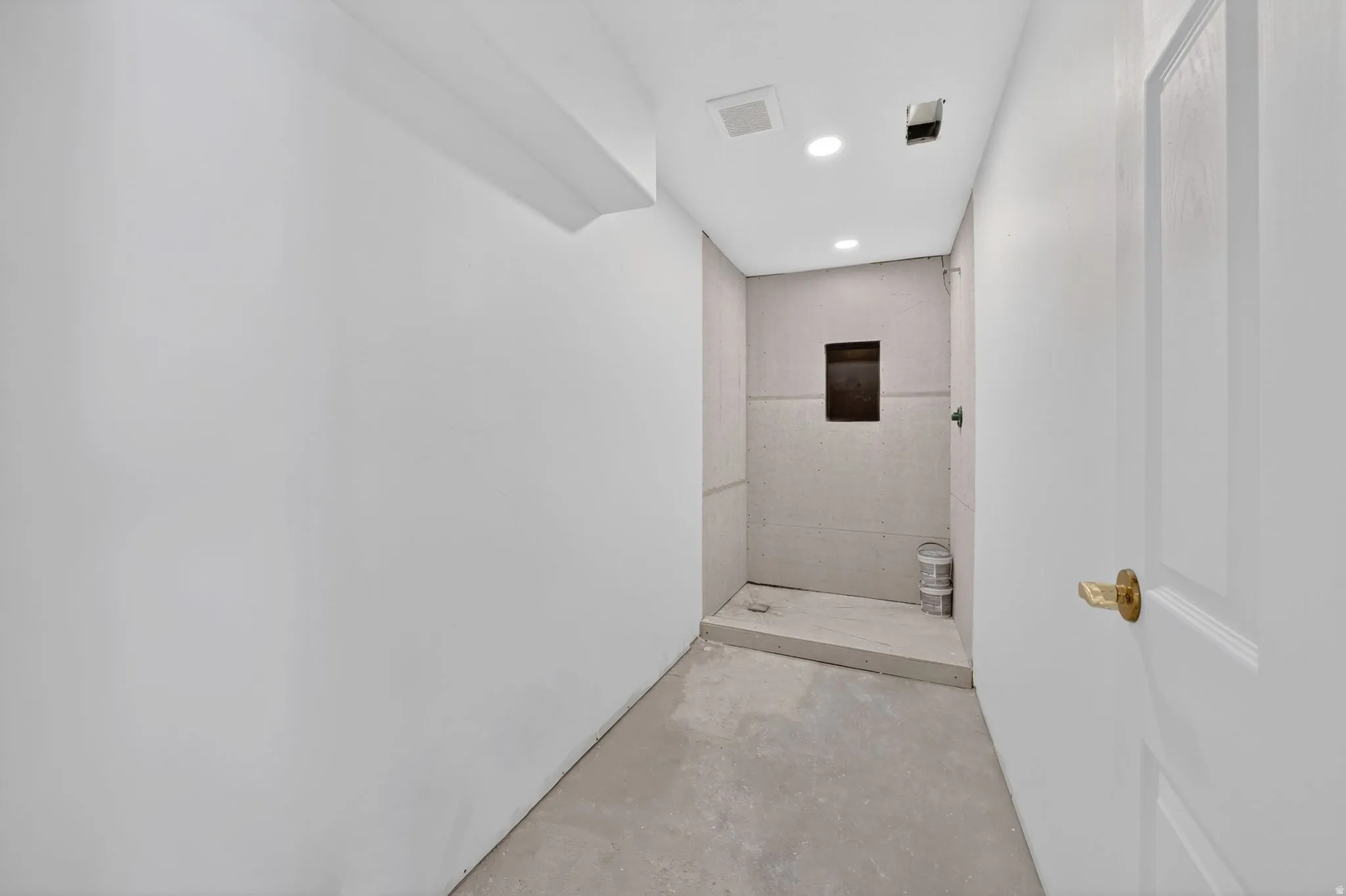 Unfinished bathroom space featuring a walk-in shower with a recessed niche, recessed lighting, and a white paneled door with brass hardware