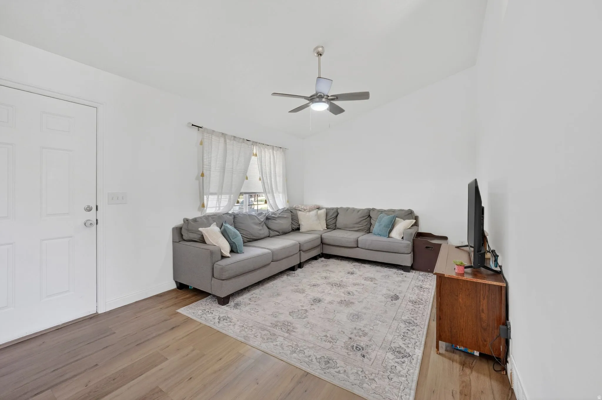Living space featuring wood-finish flooring, vaulted ceilings, a ceiling fan, and a paneled entry door