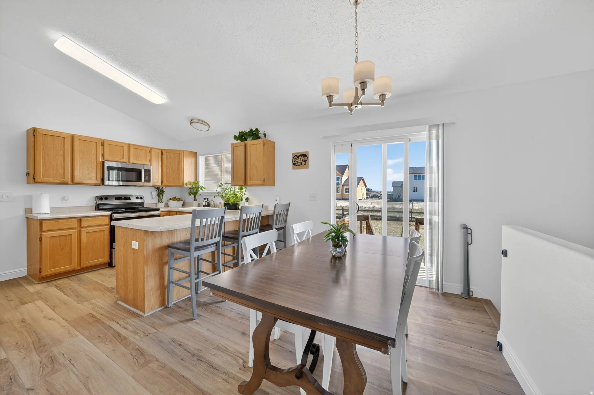 Open-concept kitchen and dining area featuring wood-finish flooring, light wood cabinetry, a center island with counter seating, stainless steel appliances, and a sliding glass door
