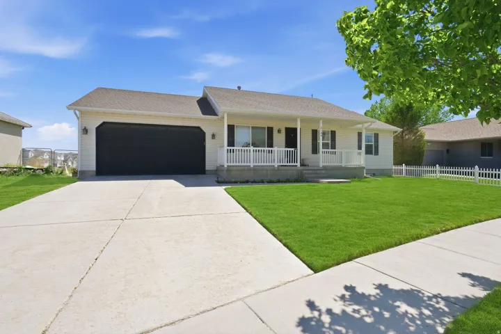 Ranch-style residence featuring a covered front porch, white picket fence, a dark garage door, and a concrete driveway