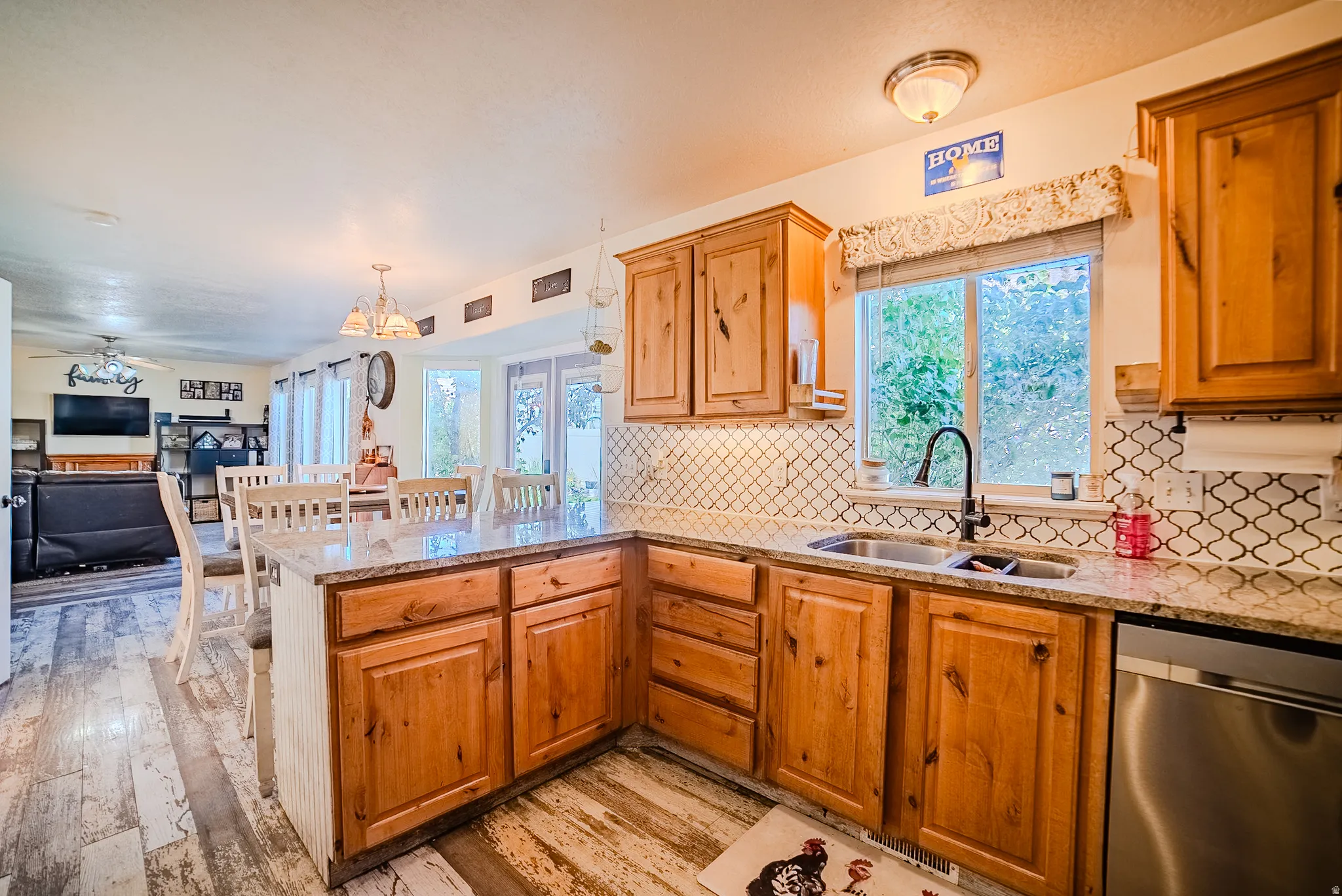 Kitchen featuring wood-finish cabinetry, granite-style countertops, a stainless steel double sink with a gooseneck faucet, and a decorative tile backsplash