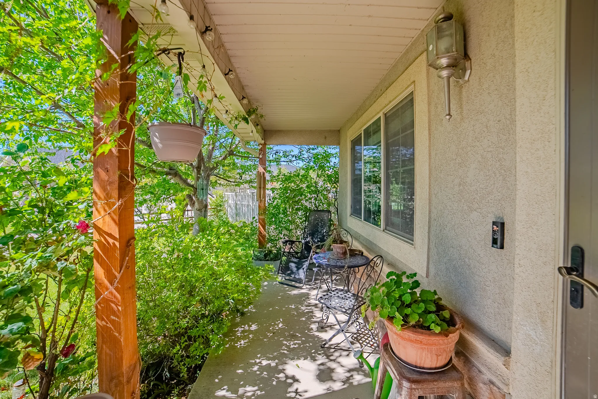 Covered front porch featuring textured stucco exterior, a large window, and an outdoor wall sconce