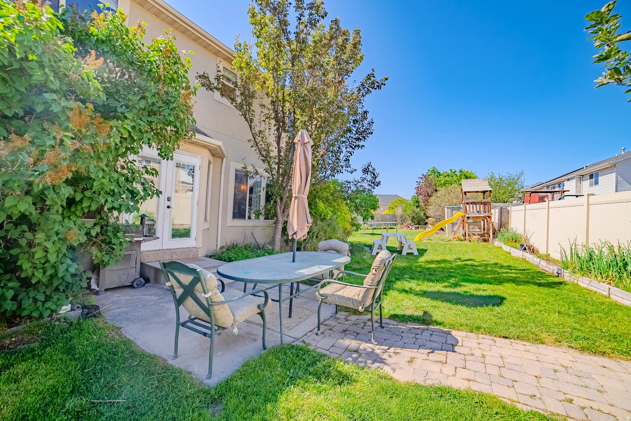 Expansive backyard featuring a paver patio with a concrete extension, manicured lawn, established landscaping, and a privacy fence
