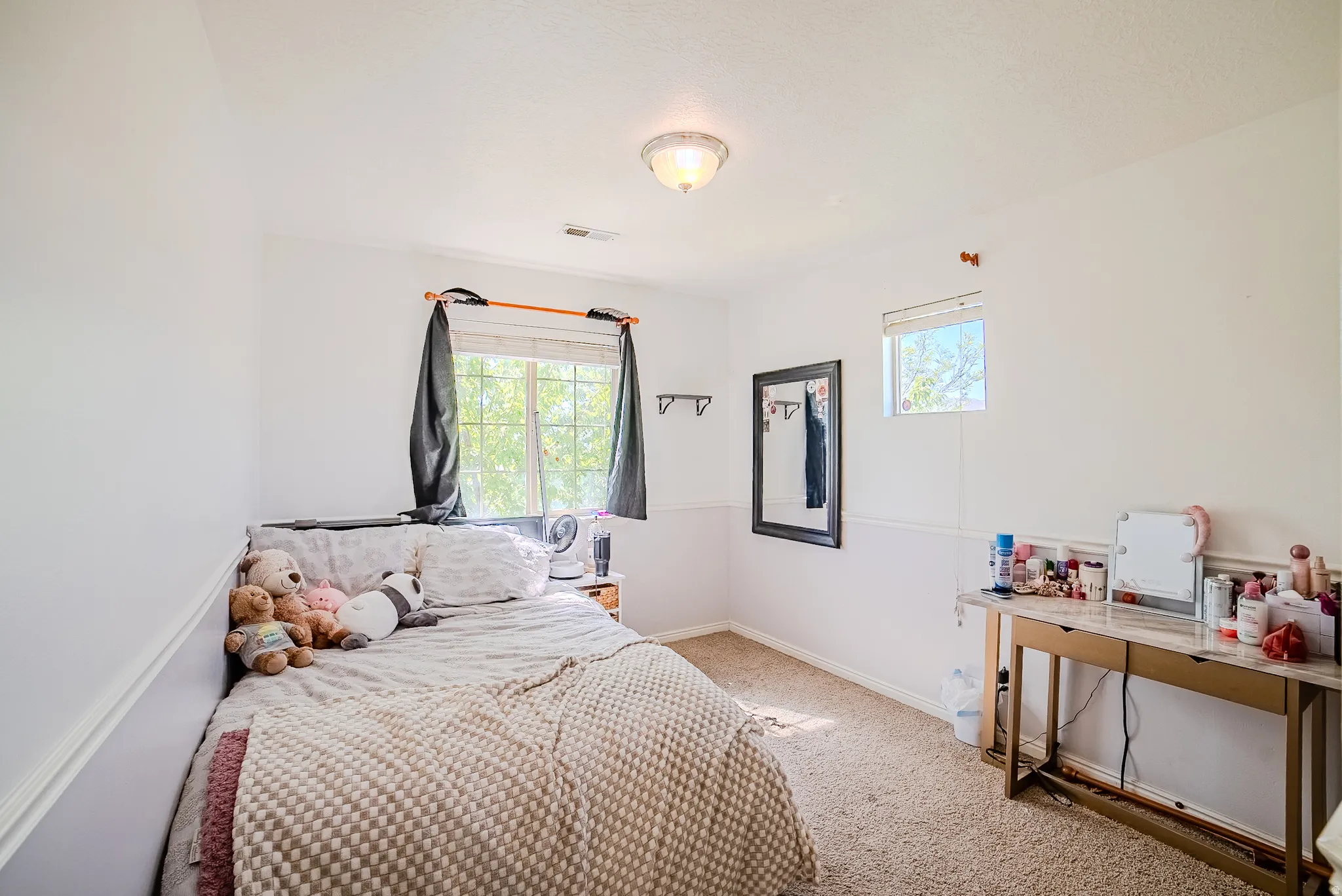 Carpeted room with a ceiling-mounted light fixture, two windows, and white walls featuring wainscoting