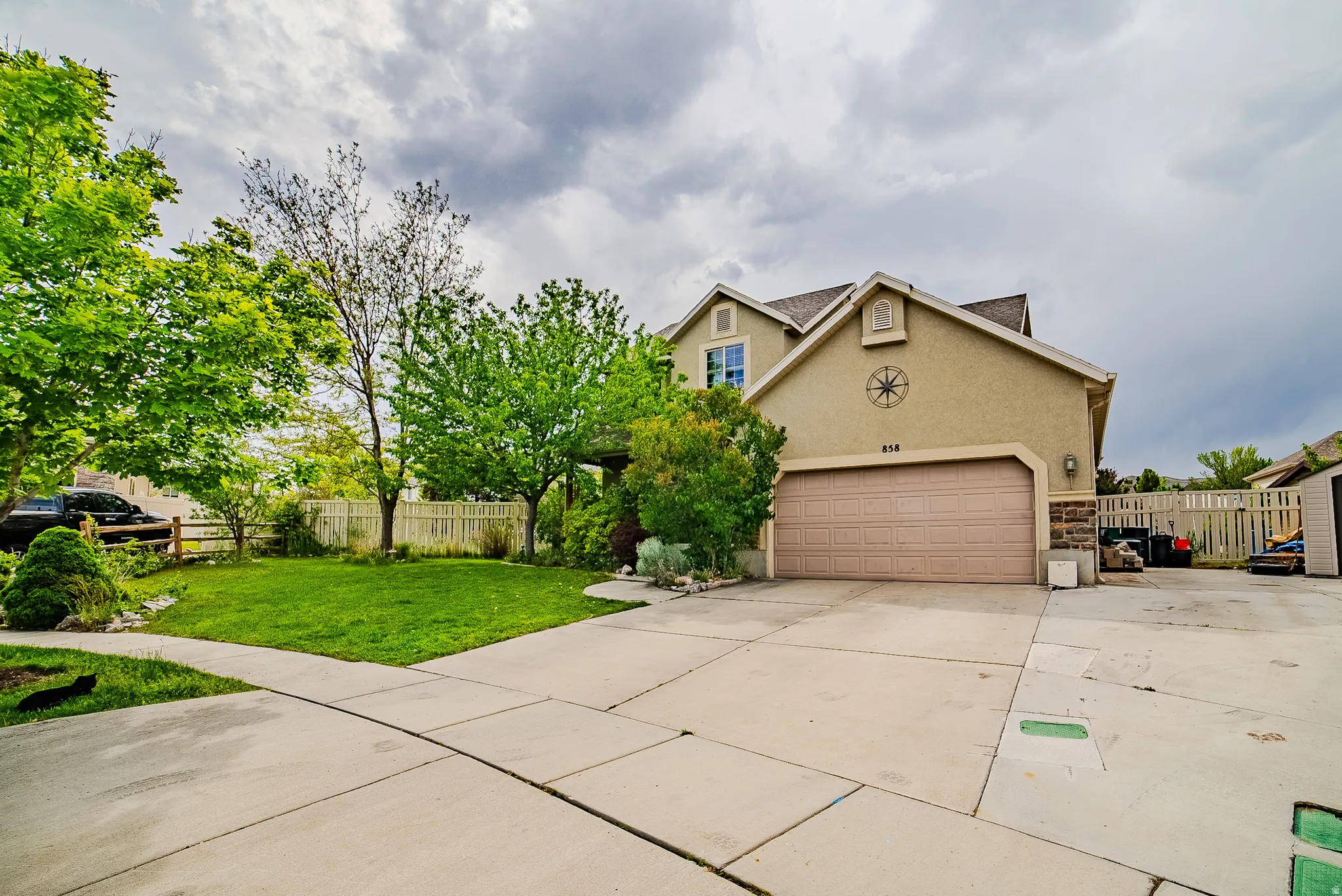 Stucco exterior residence featuring an attached garage with a panel door, a concrete driveway, and a front lawn with mature trees and shrubs