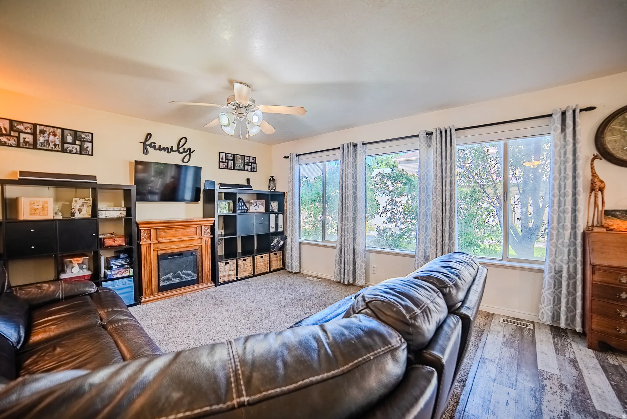 Living area featuring a ceiling fan, light-toned walls, and a wood-finish fireplace with an electric insert