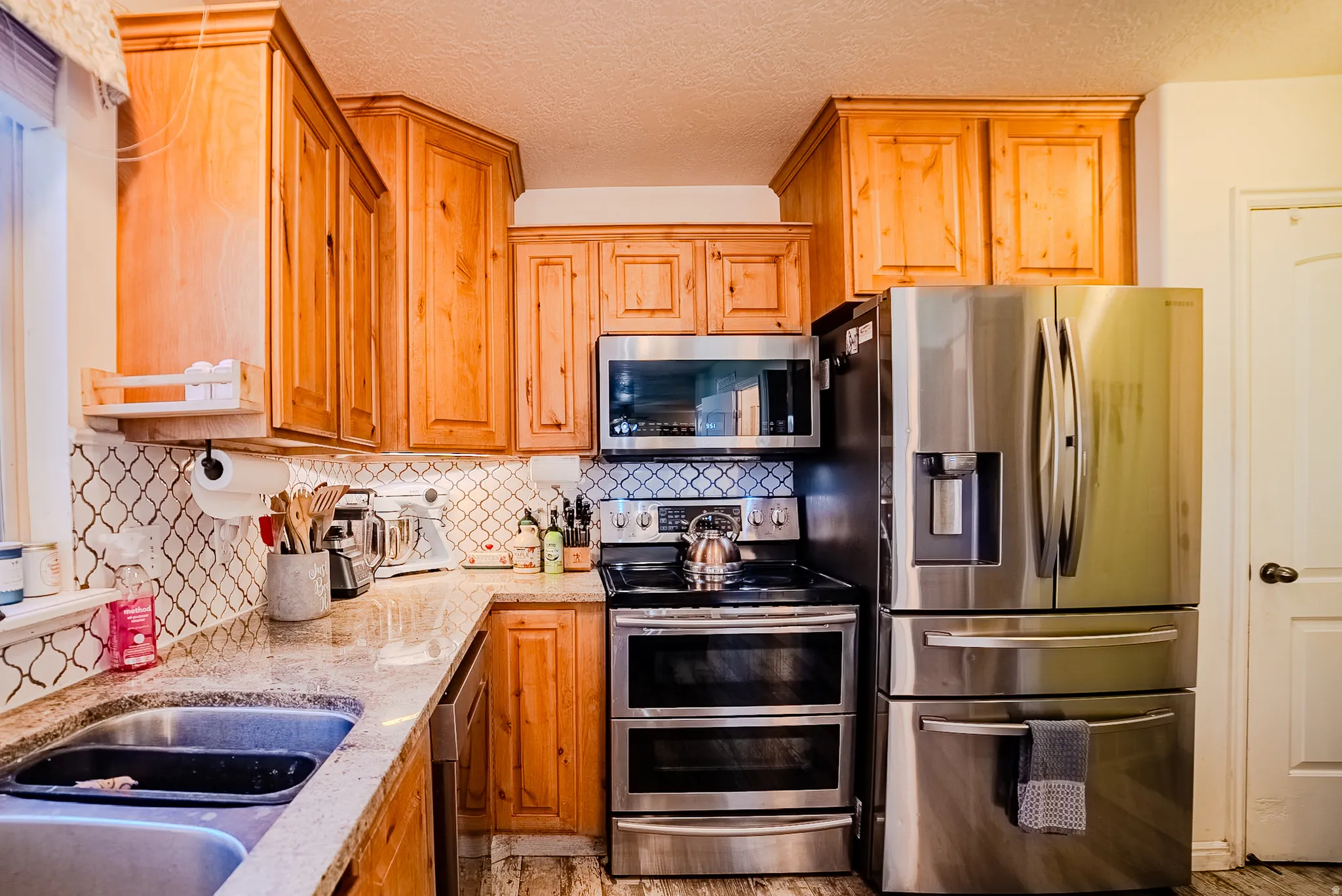 Kitchen featuring light wood cabinetry, light-colored countertops, a tile backsplash, and stainless steel appliances