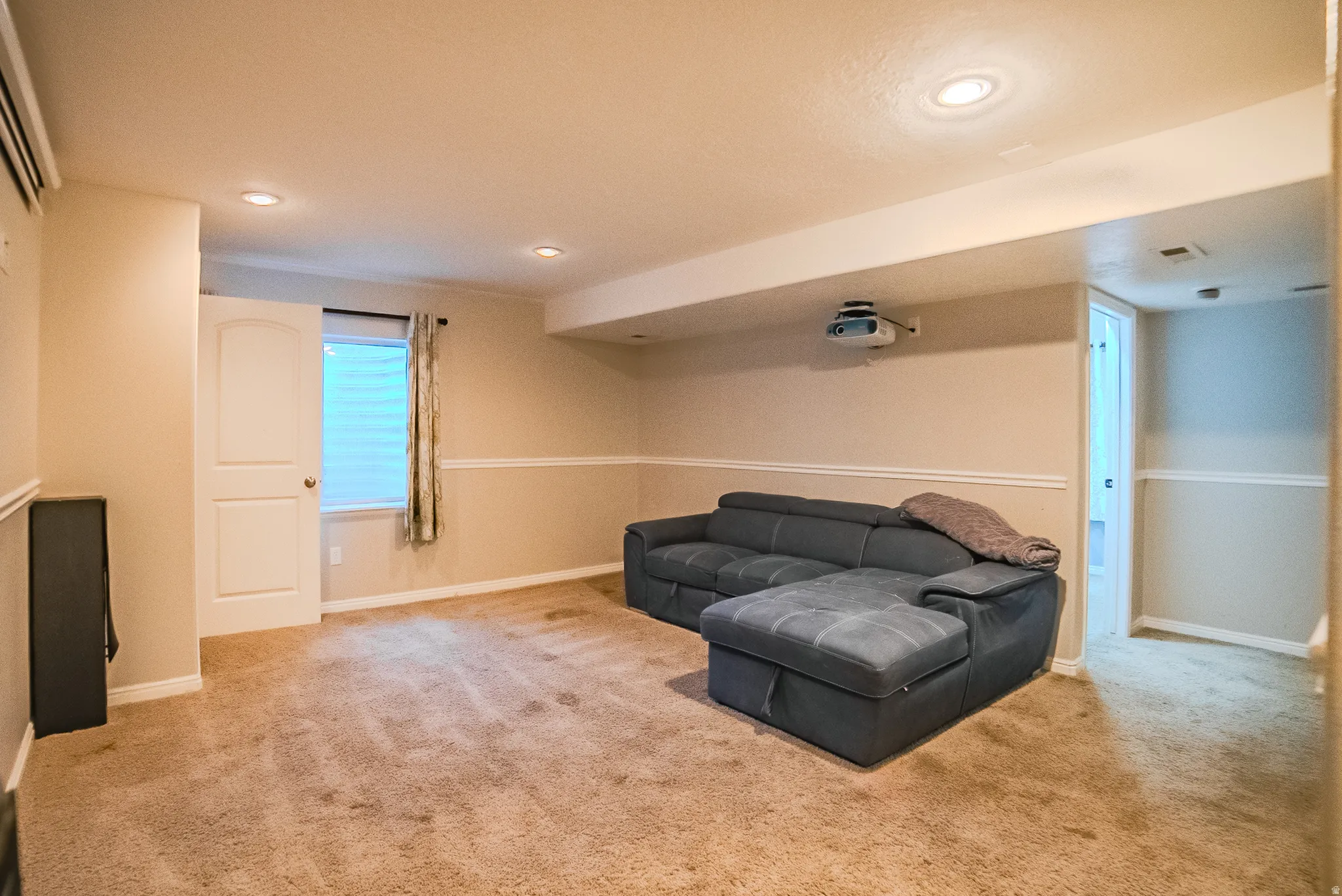 Carpeted interior space featuring recessed lighting, a mounted projector, and a window with blinds