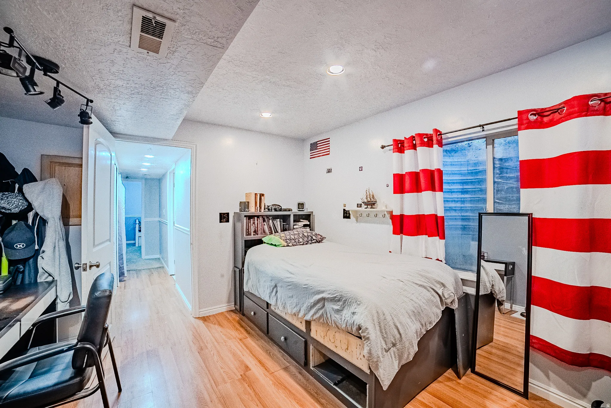 Bedroom featuring wood-finish flooring, a track lighting fixture, and a window with a built-in shelf below