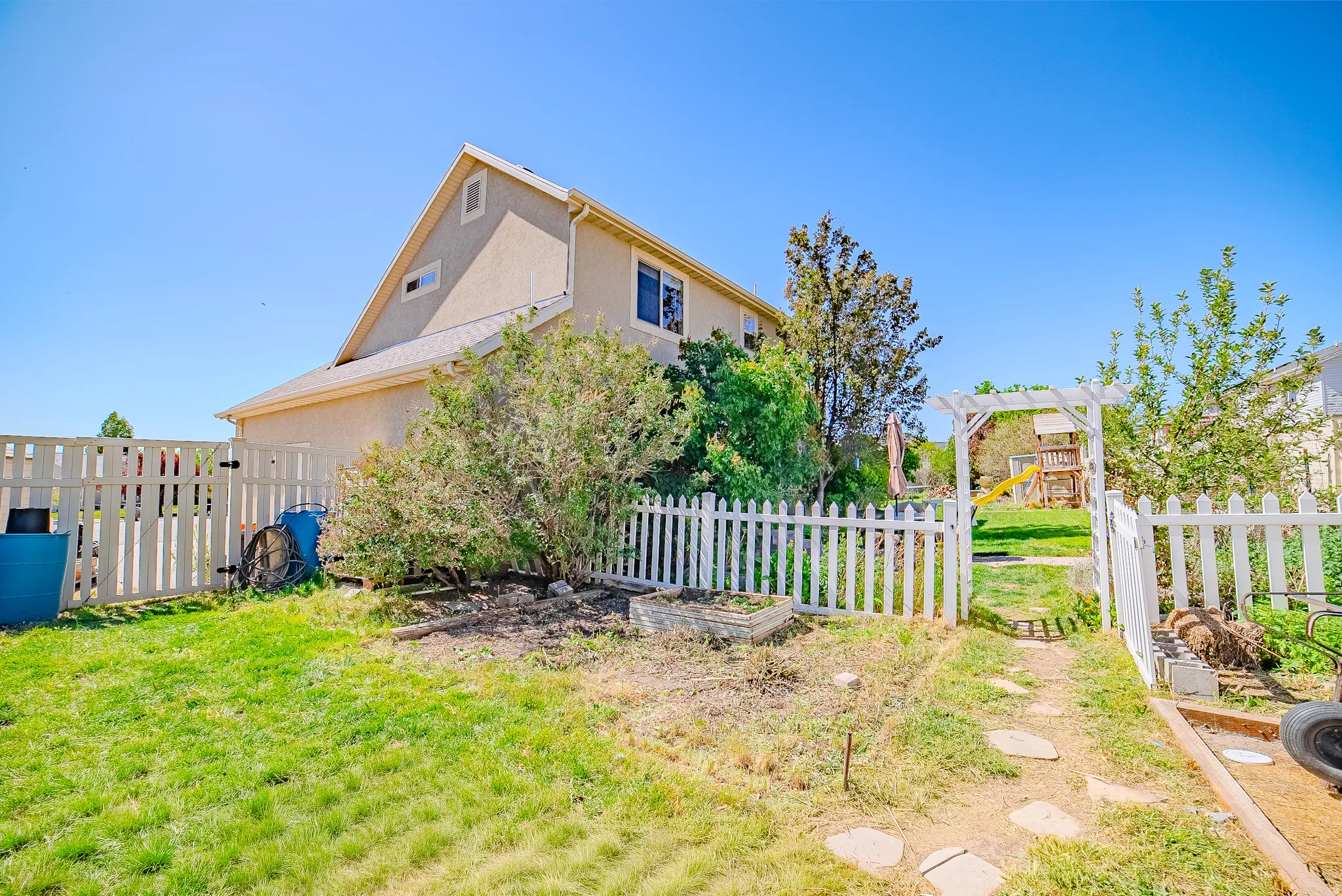 Spacious backyard with a white picket fence and a stone path leading through a white pergola