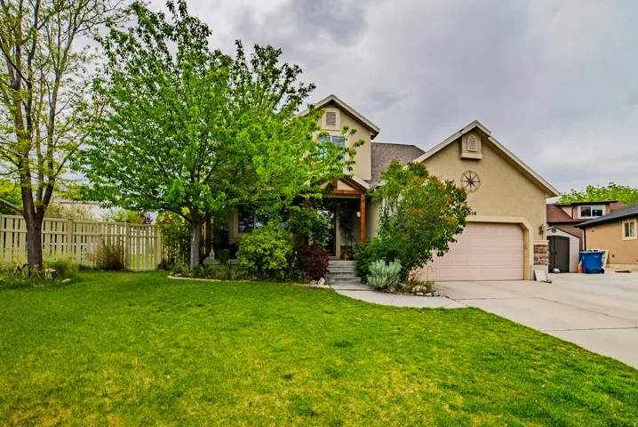 Two-story stucco residence featuring a covered entry, an attached garage with a light-toned door, mature trees, and a well-maintained lawn