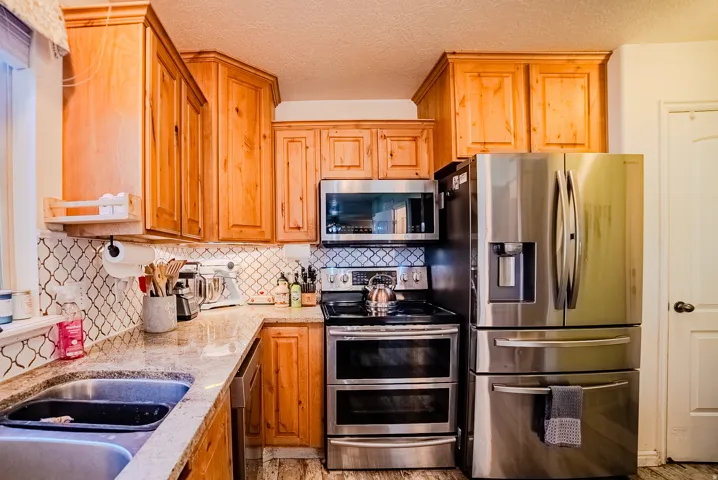 Kitchen featuring light wood cabinetry, light-colored countertops, a tile backsplash, and stainless steel appliances